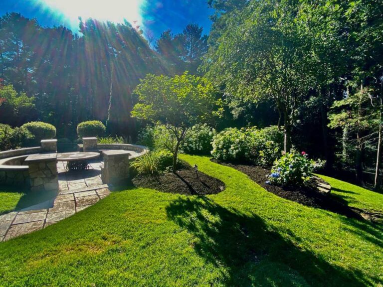 Maione Landscapes project showcasing a beautifully designed backyard with green lawn, colorful flowers, and a patio area with comfortable outdoor furniture
