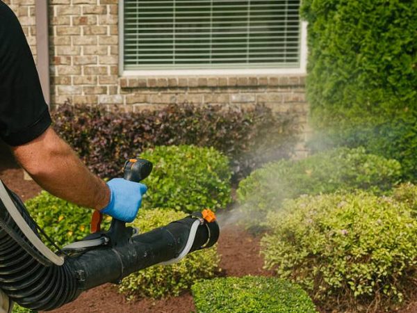 A person wearing protective clothing to apply mosquito control treatment in a residential backyard